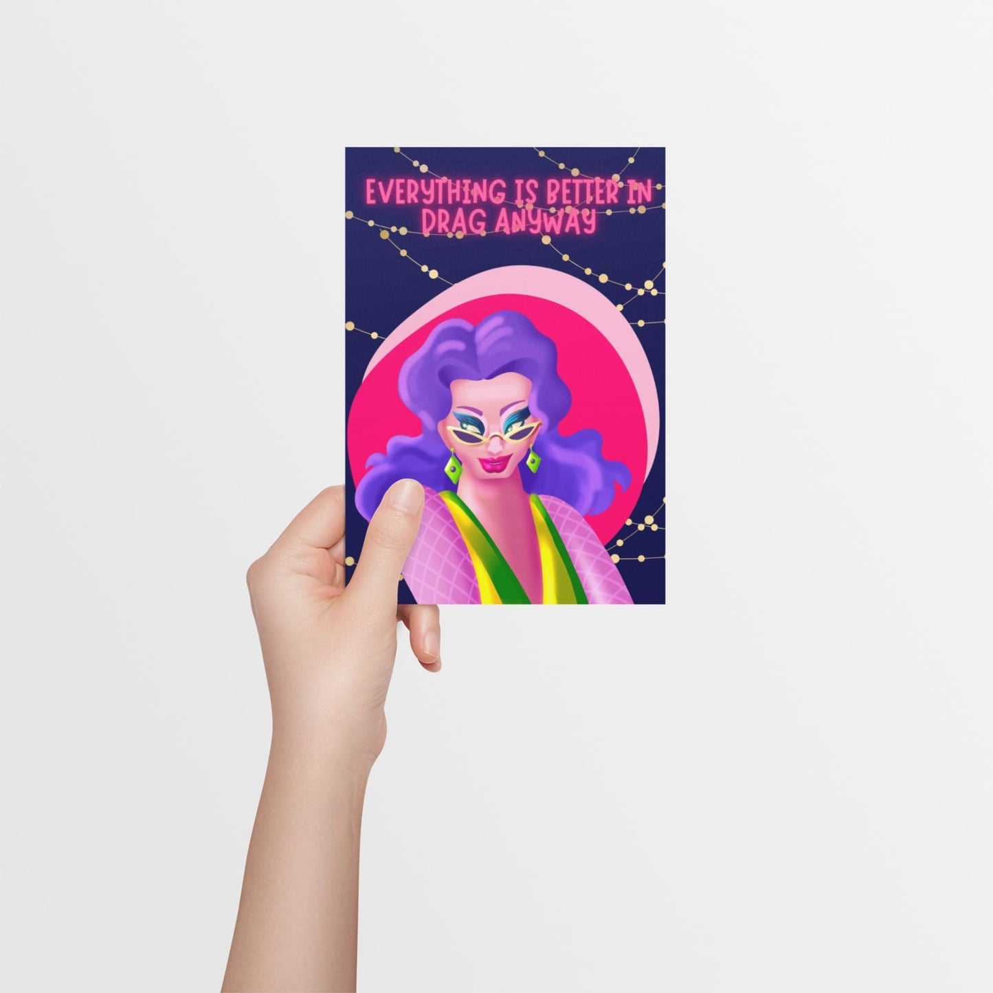 A hand holding a card, with a dark blue background and fairy lights featuring a drag queen dressed in bright colours in a sassy pose. Designed to support and celebrate drag artists.